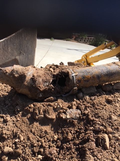 A broken pipe is laying in the dirt next to a yellow excavator