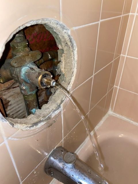 A bathroom with a hole in the wall and water coming out of it.