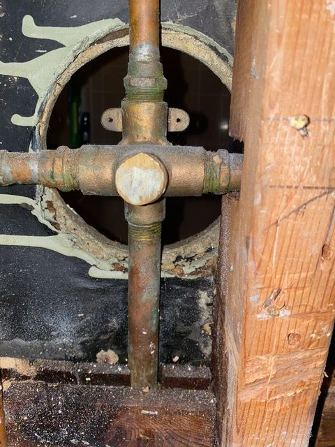 A close up of a copper pipe with a hole in the wall