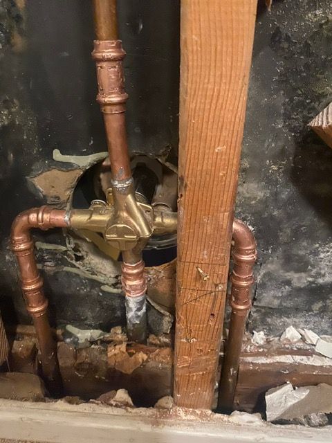 A close up of a copper pipe in a hole in a wall.