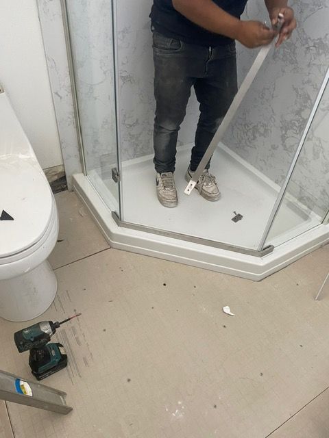 A man is working on a shower stall in a bathroom.