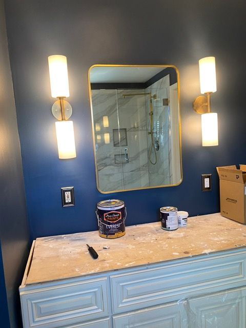 A bathroom with blue walls , a sink , a mirror and two lights.