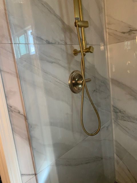 A shower with a marble wall and a brass shower head.