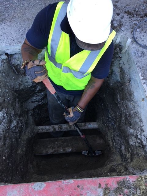 A man wearing a hard hat and safety vest is digging in a hole