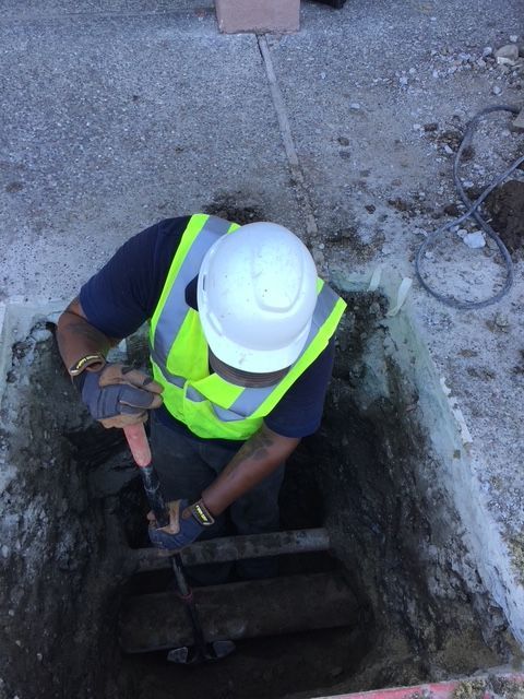 A man wearing a hard hat and safety vest is digging in a hole