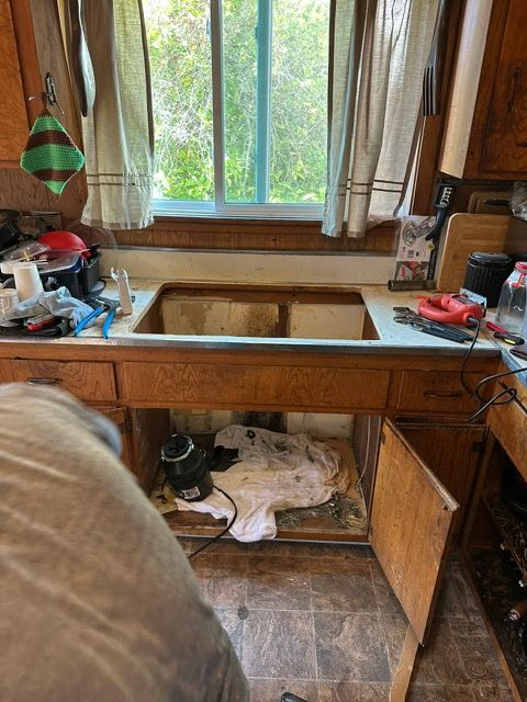 A person is working on a kitchen sink under a window.