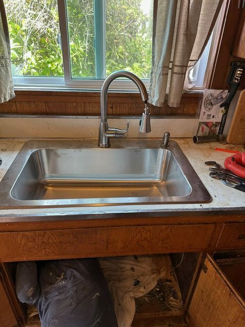 A stainless steel kitchen sink is under a window in a kitchen.