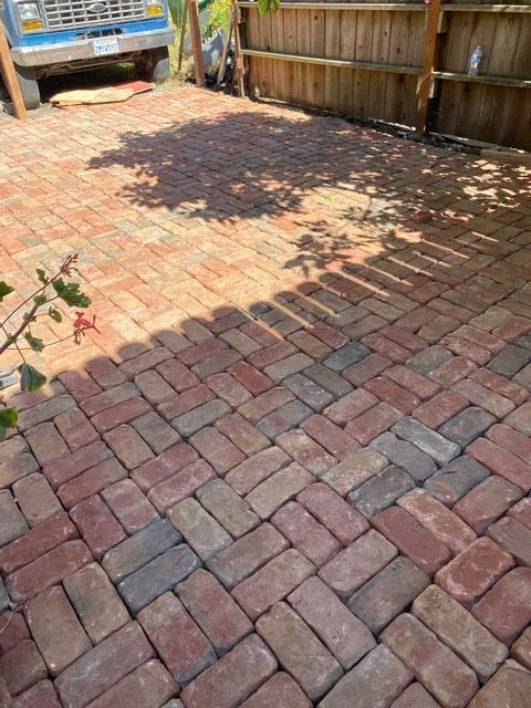 A brick driveway with a blue truck parked in the background.