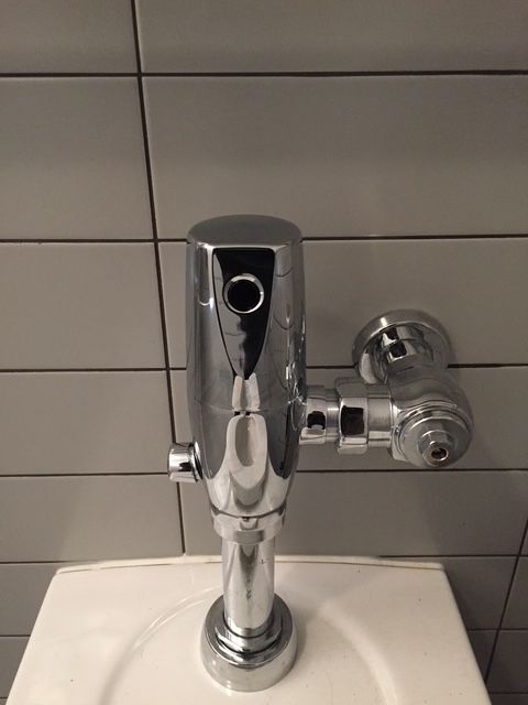 A close up of a toilet flush valve in a bathroom
