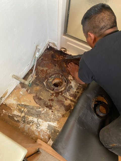 A man is kneeling on the floor looking at a hole in the floor.