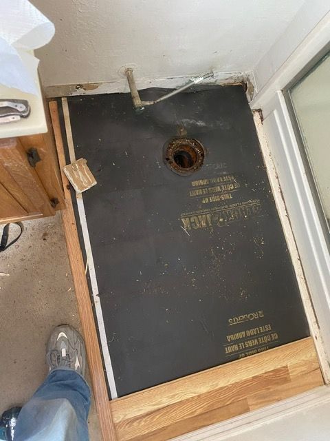 A person is standing on a wooden floor next to a shower stall.