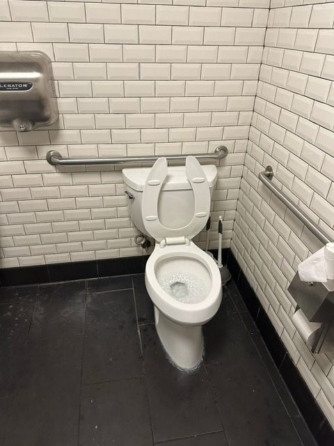 A toilet in a public restroom with white brick walls