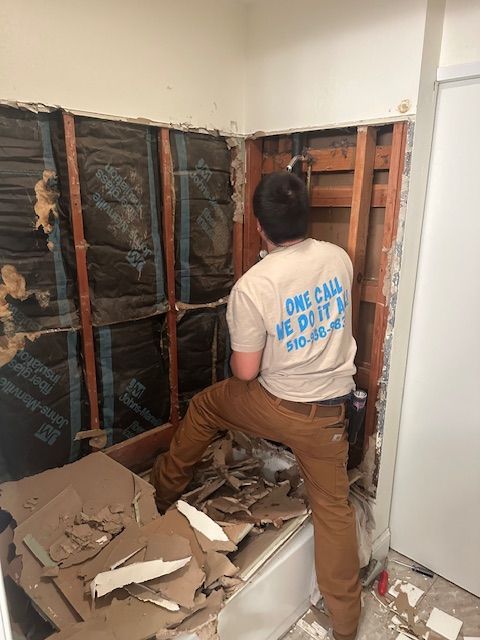 A man wearing a shirt that says `` one call we do it '' is working in a bathroom.