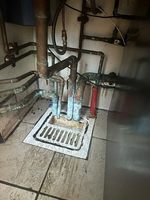 A dirty bathroom with a drain and pipes