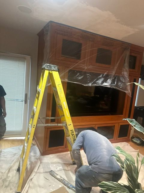 A man is kneeling down in front of a yellow ladder in a living room.
