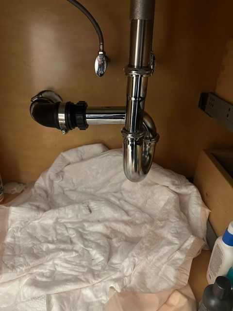 A sink with a pipe underneath it and a towel on the floor.