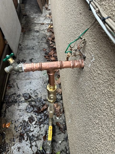 A copper pipe is attached to a wall with a green valve.