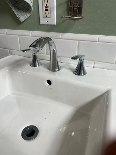 A bathroom sink with three faucets and a drain.