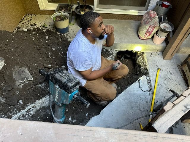 A man is kneeling down in the dirt with a hammer.
