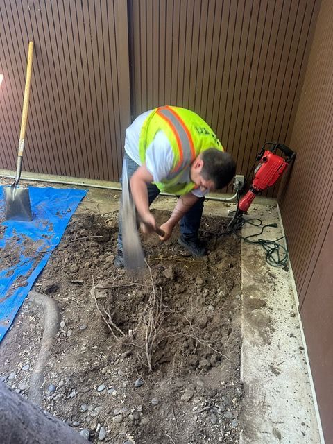 A man in a yellow vest is digging in the dirt