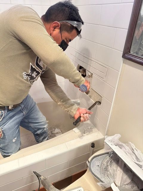 A man wearing a mask is working on a bathtub in a bathroom.