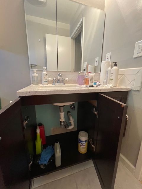 A bathroom with a sink , mirror and cabinets open