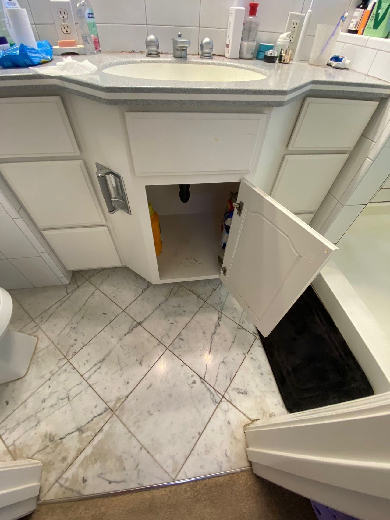 A bathroom with a sink , toilet , and cabinets with the door open.