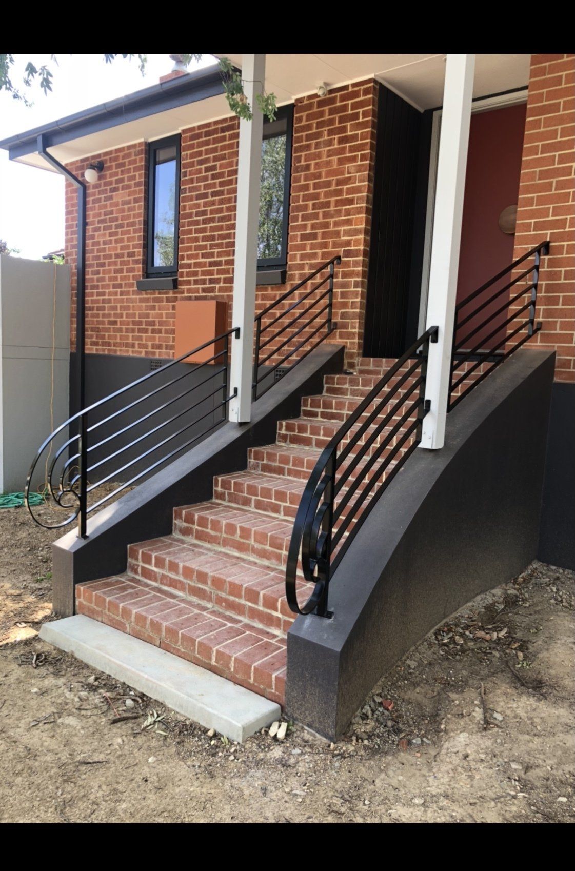 A brick house with stairs and a black railing.