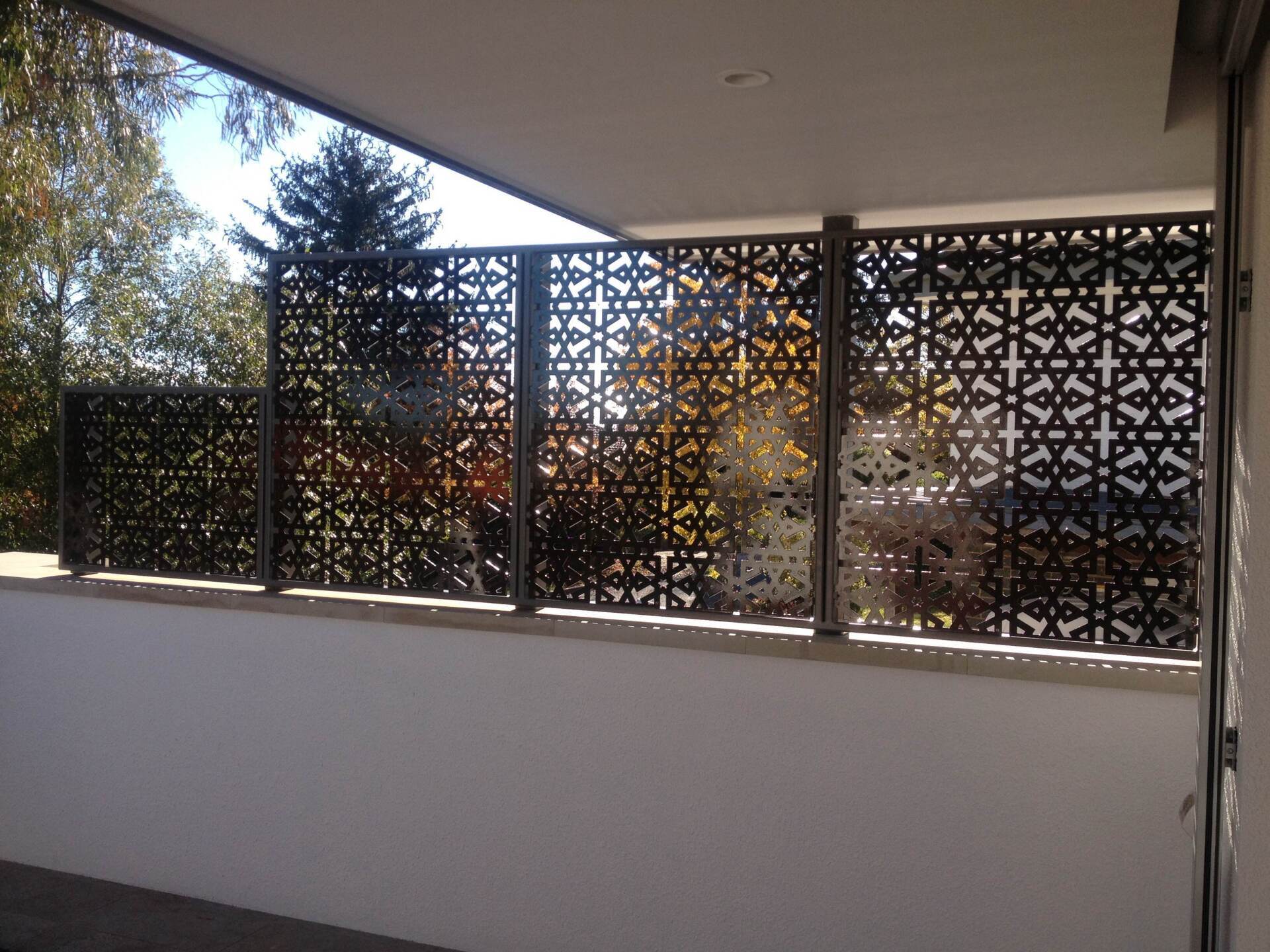 A balcony with a metal fence and a window with trees in the background.