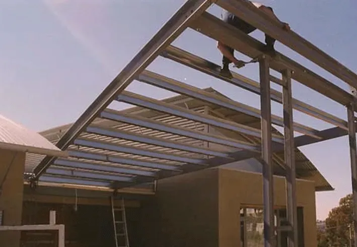 A man is working on a metal structure in front of a house.