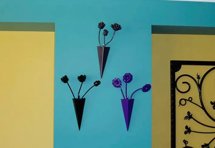 Three metal vases hanging on a wall with flowers in them