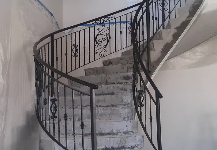 A spiral staircase with a wrought iron railing in a building under construction.