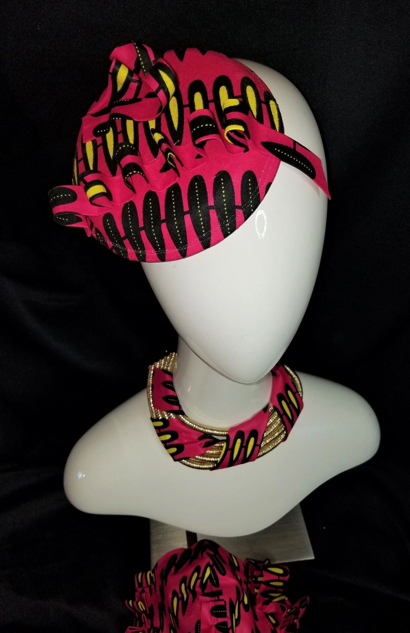 Mannequin head with pink and yellow patterned headband and necklace; black background.