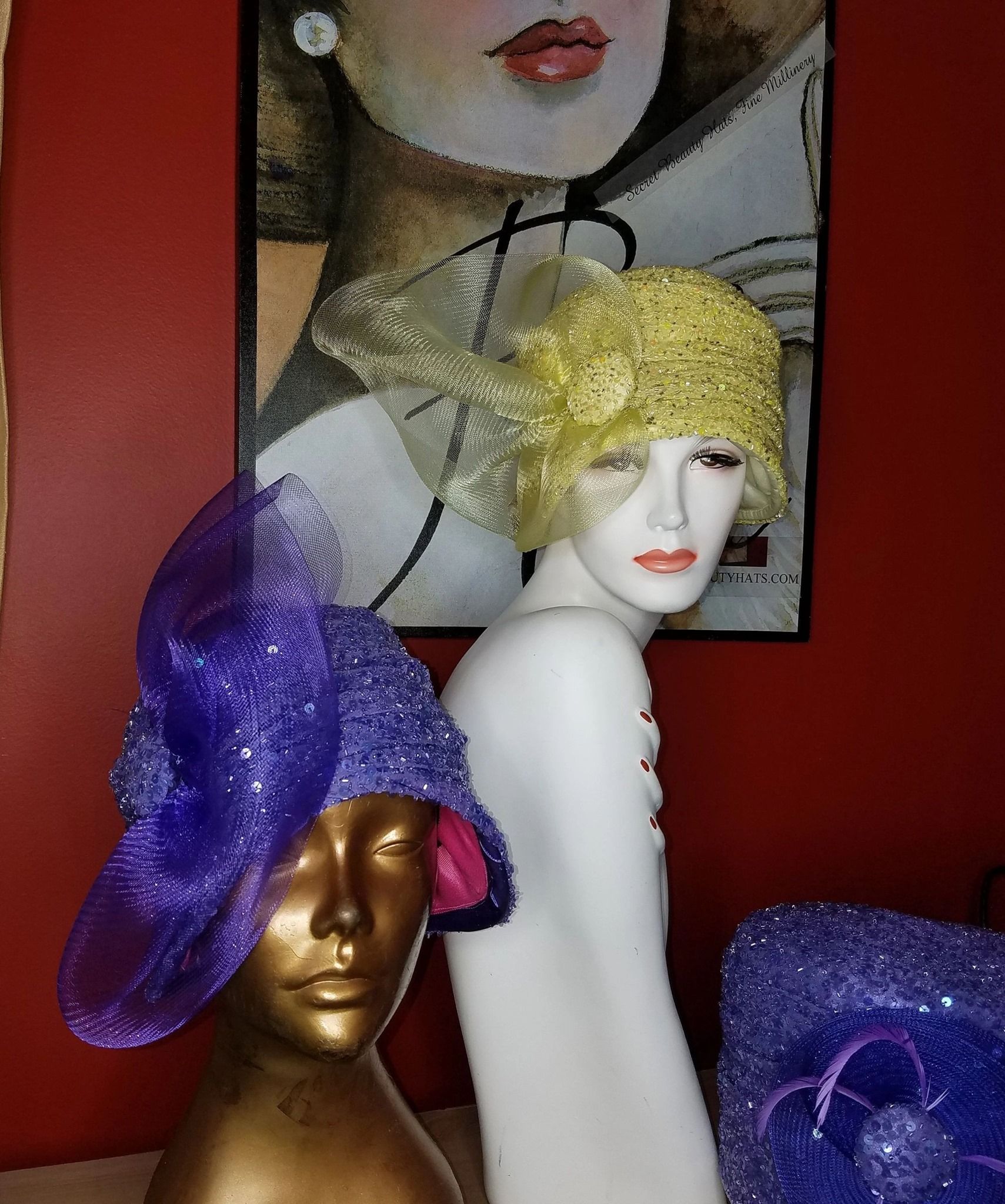 Display of hats on mannequins: purple and gold hats; red background with a painting.