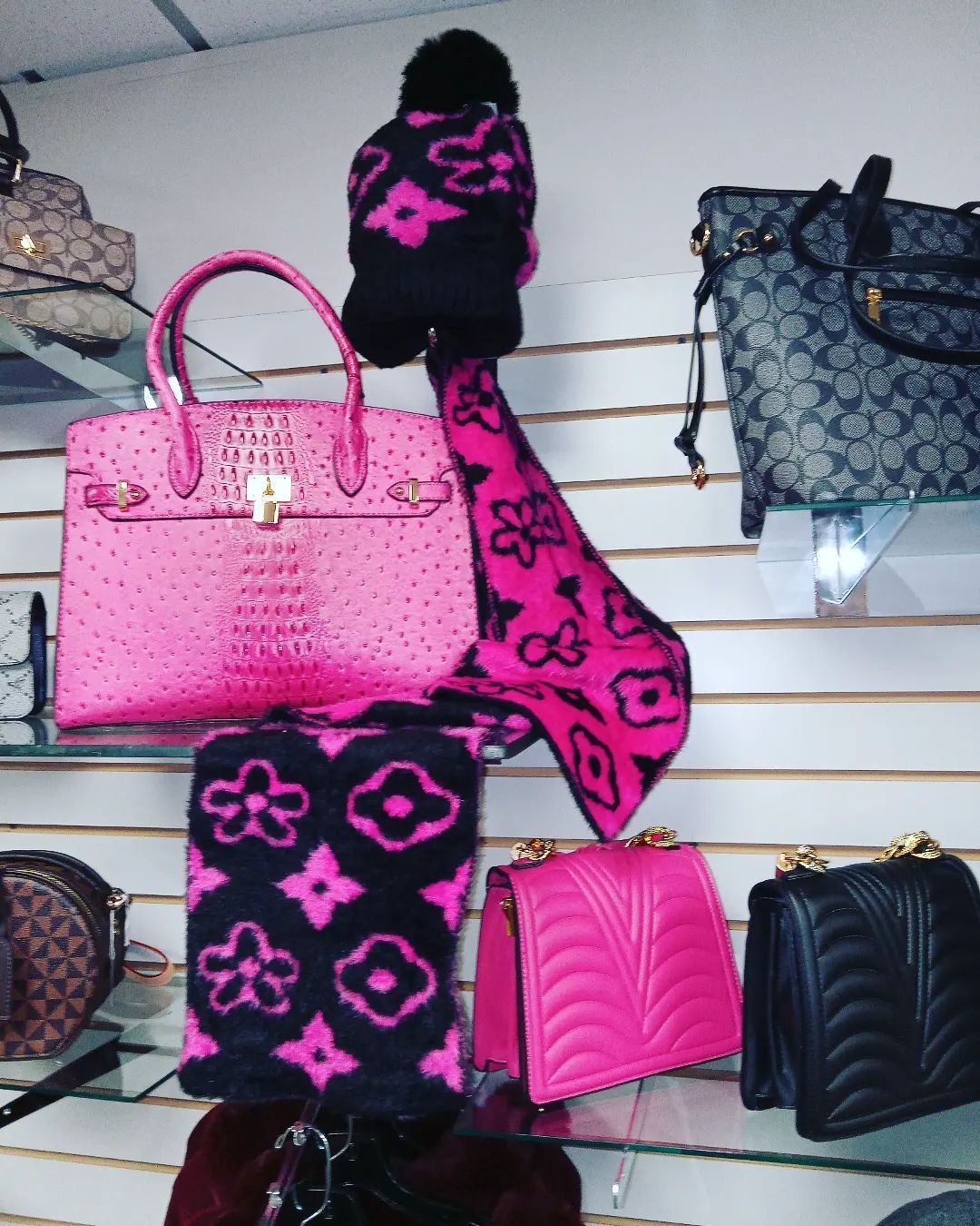 Display of pink handbags and matching hat/scarf set on a shelf, in a store setting.
