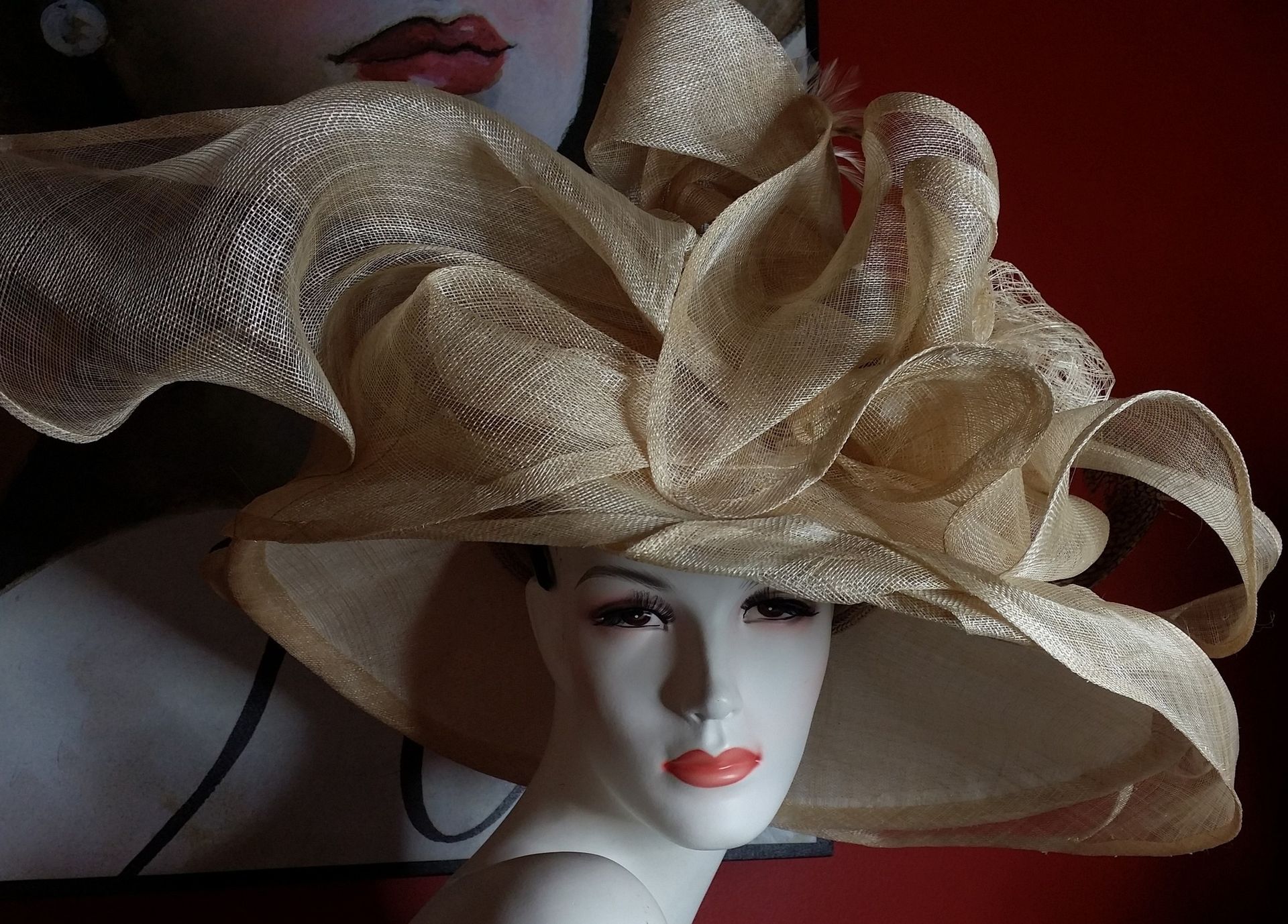 Mannequin wearing a large, gold, ruffled sun hat against a red wall.