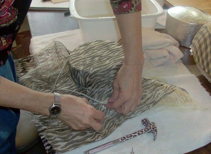 Person working with fabric and hat, white thread, table, hammer, water basin.