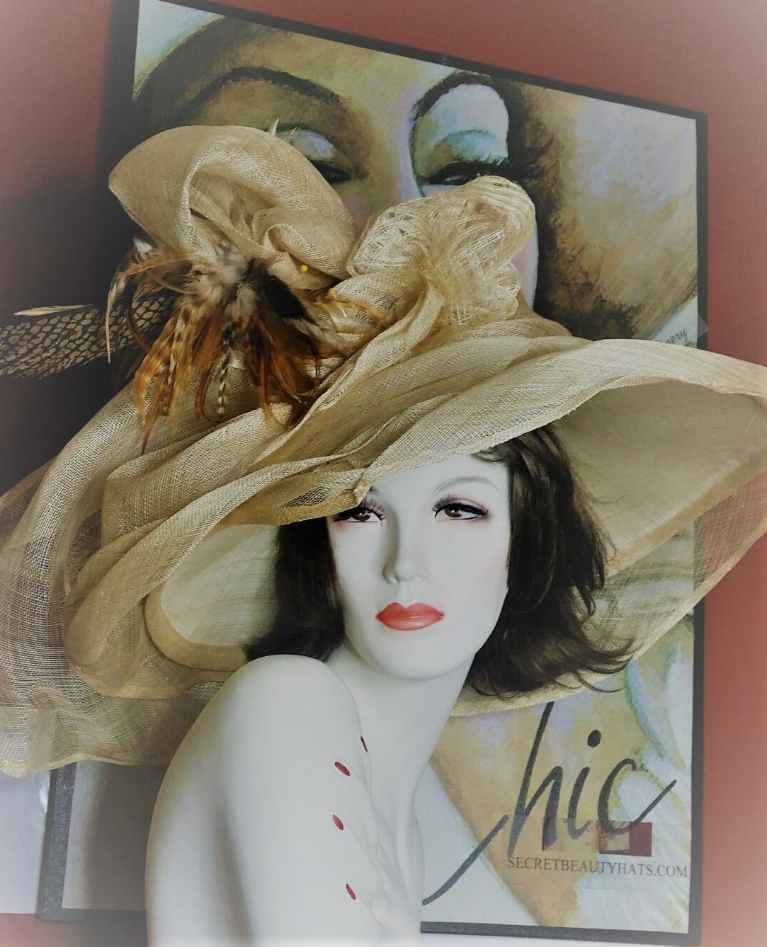 Mannequin wearing a wide-brimmed gold hat, in front of a painting.
