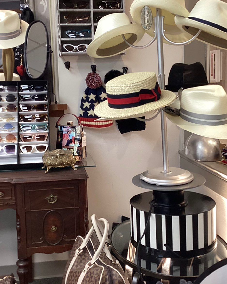 A room displaying hats and sunglasses on shelves and a hat stand, alongside a wooden desk.