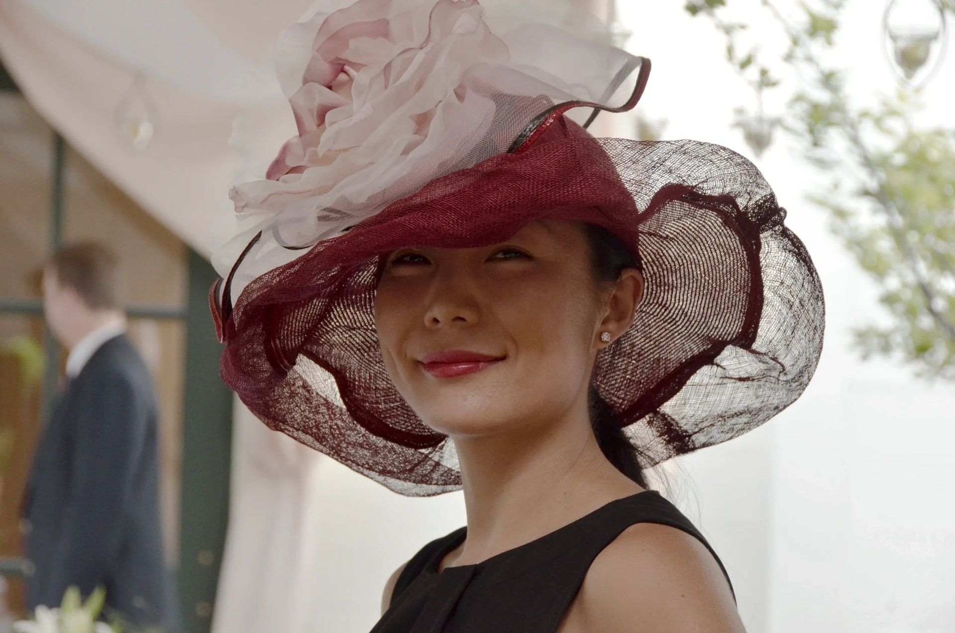Woman wearing a large burgundy and white hat smiles outside.
