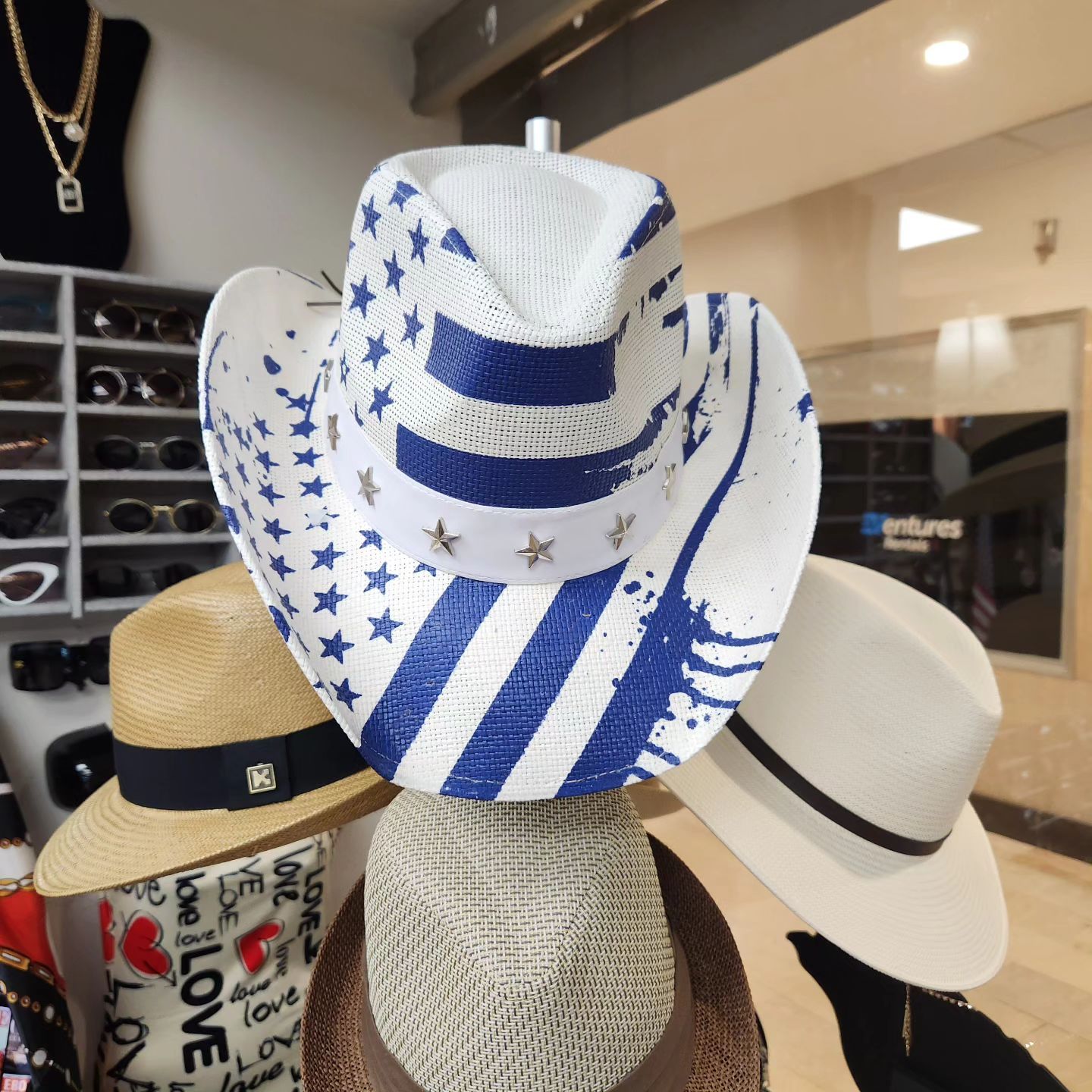 Hats displayed on a mannequin. Patriotic cowboy hat, straw hat with black band, and white hat. Store interior.