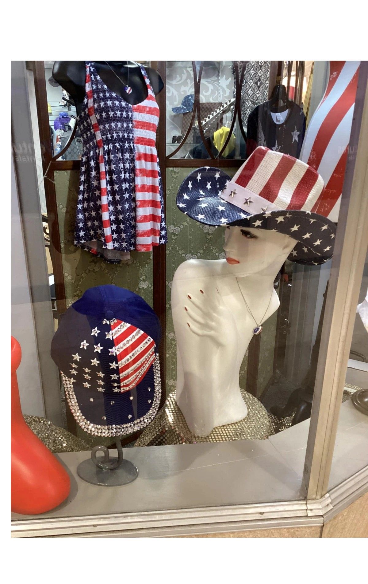 Window display with patriotic-themed hats and clothing, including a dress, on mannequins.