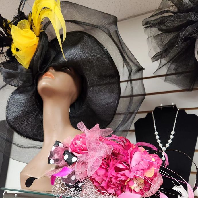 Mannequin in black hat with yellow feathers; pink floral fascinator; necklace.