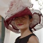 Woman wearing a wide-brimmed hat with maroon and white fabric, smiling, outdoors.