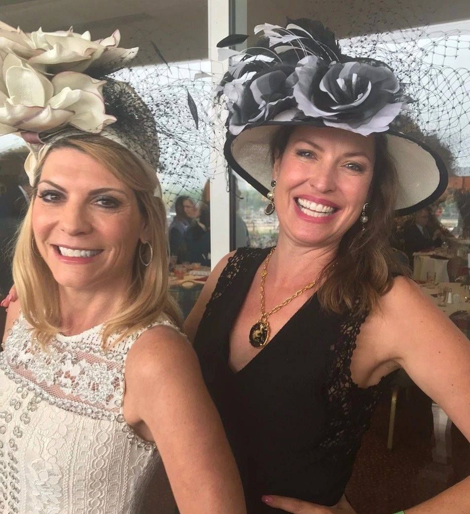 Two women smiling, wearing elaborate hats with floral and netting details.