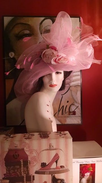 Mannequin wearing a large pink hat, with a poster and gift box in the background.
