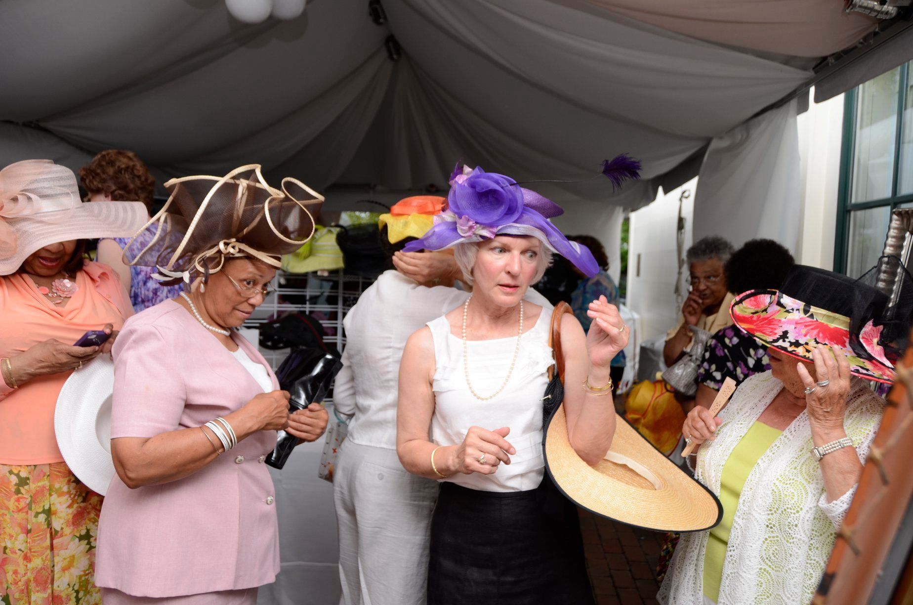 People wearing elaborate hats inside a tent, likely at an event.