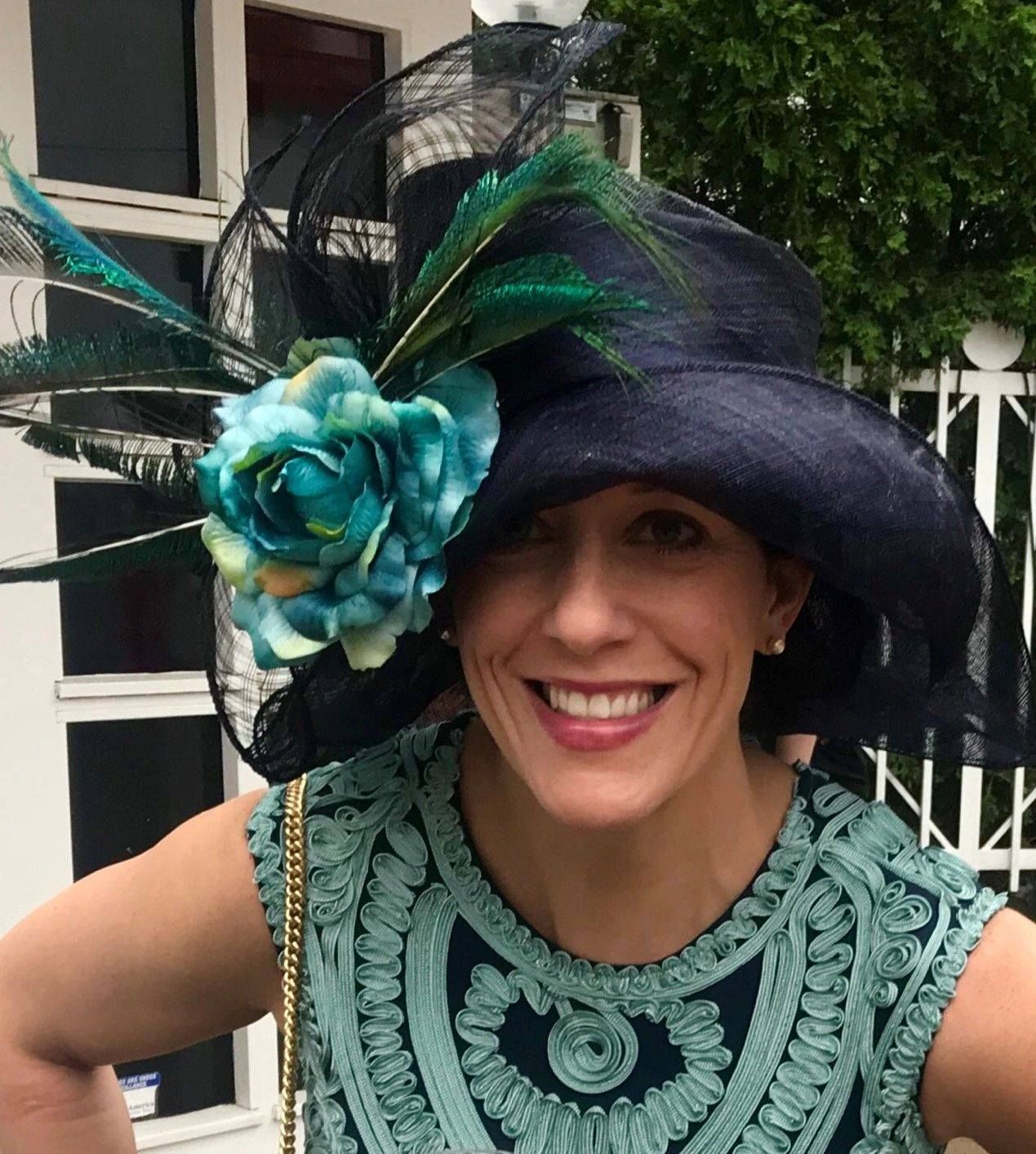 Woman smiling, wearing a navy hat with teal accents, matching teal patterned dress, outdoors.