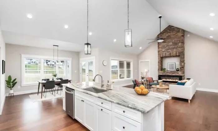 Open-concept living space with kitchen island, dining table, and stone fireplace, with wood floors.