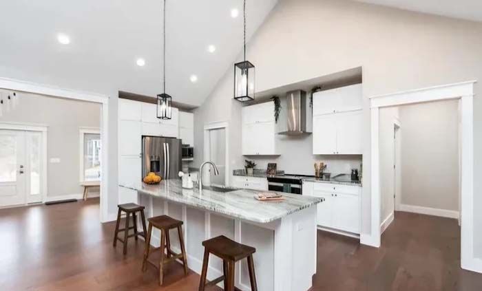 Modern white kitchen with island, stainless steel appliances, and dark wood floors.